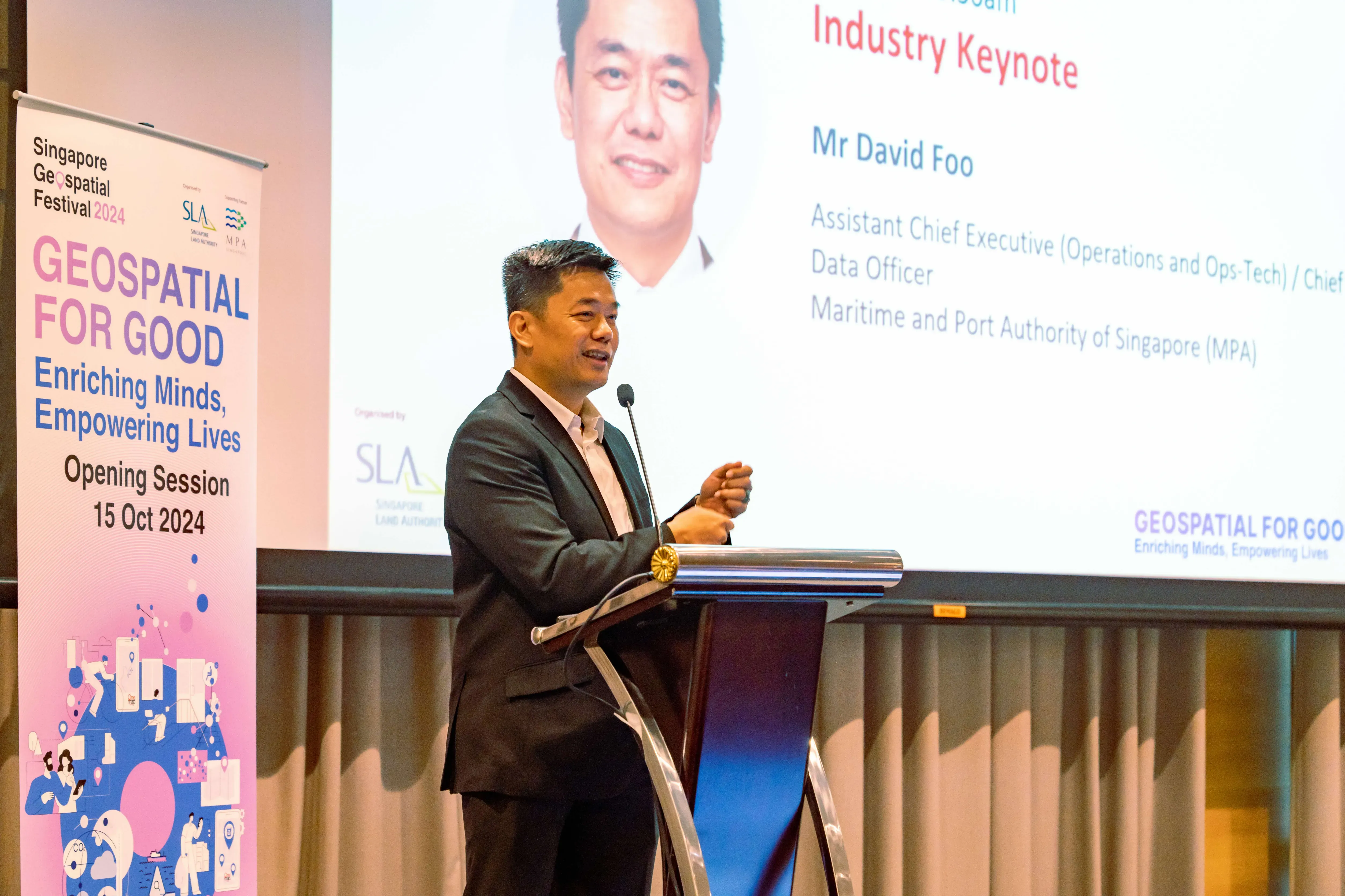 Man in dark suit speaking at podium during Singapore Geospatial Festival 2024, with a slide showing Industry Keynote by Mr David Foo.